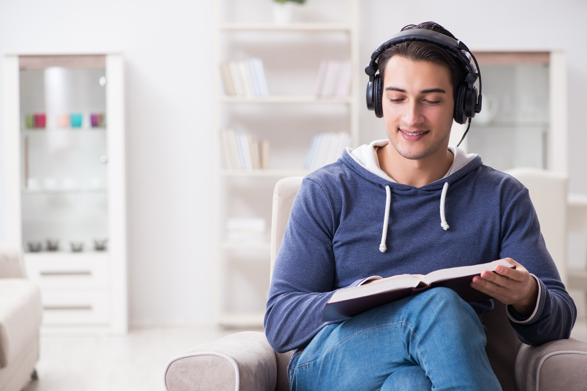 Young Man Reading Book and Listening to Audio Book